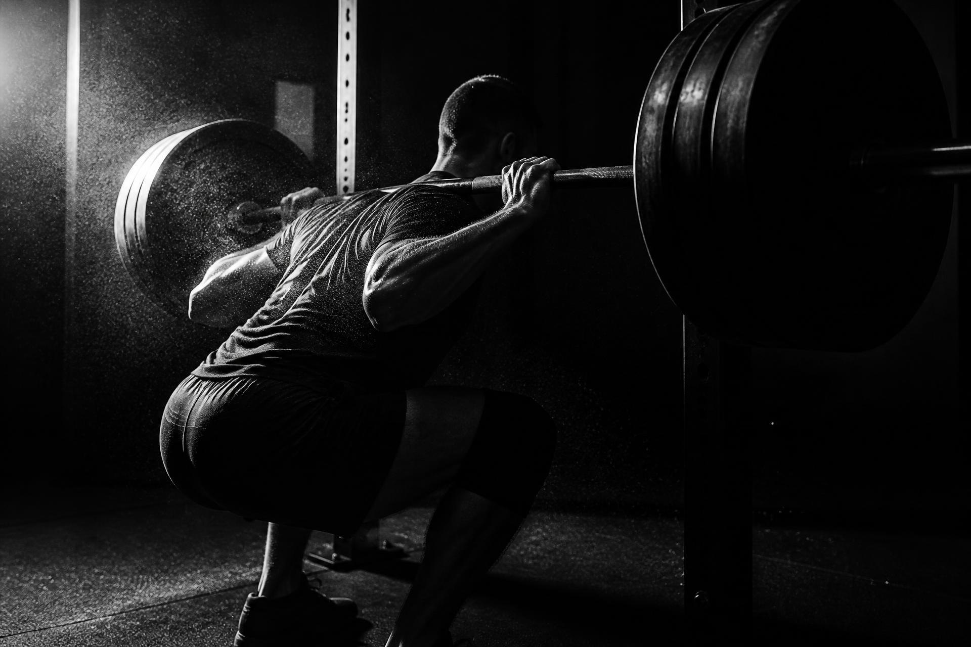 Athlete performing a heavy barbell back squat in a moody private training studio